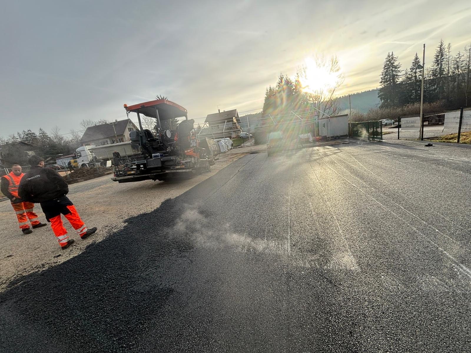 Finisseur HCE posant l'enrobé à chaud à 160°C, vapeur visible au coucher de soleil